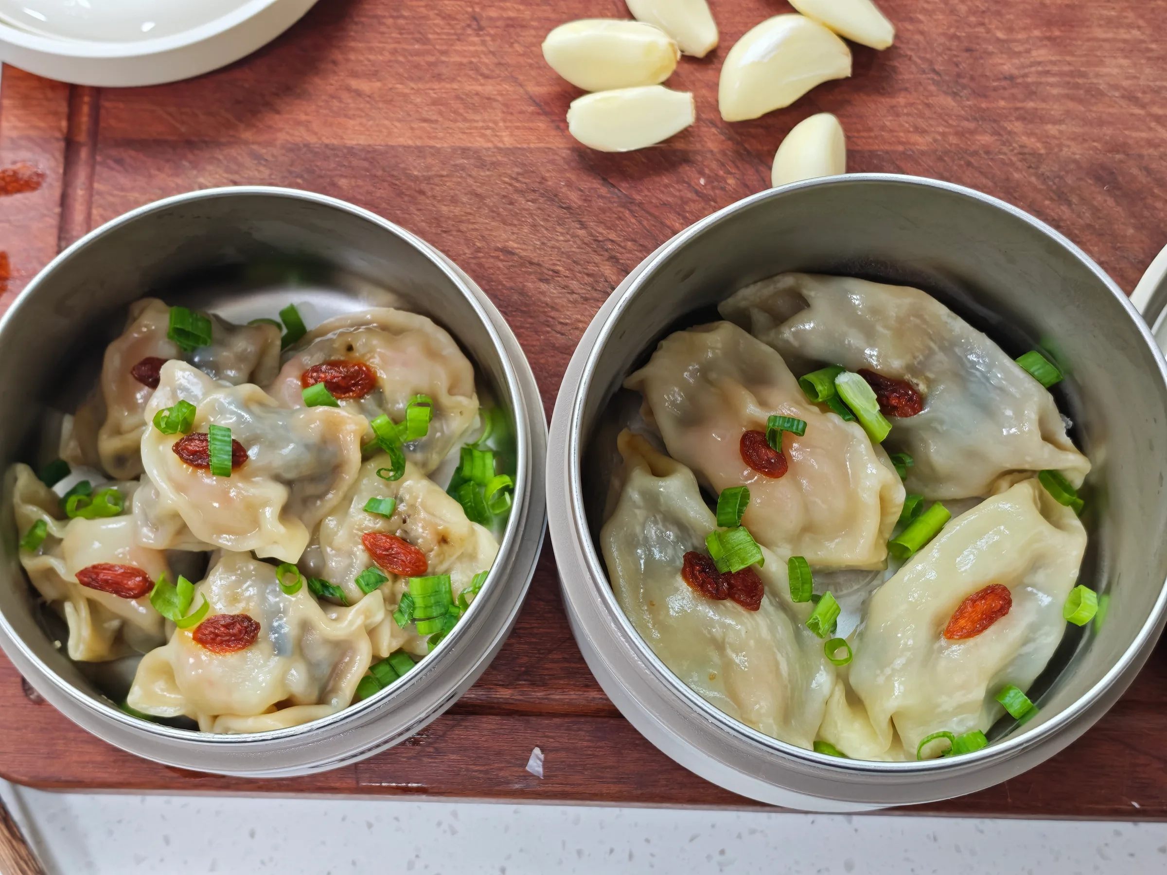 Two bowls of steamed dumplings topped with spring onion and goji berries