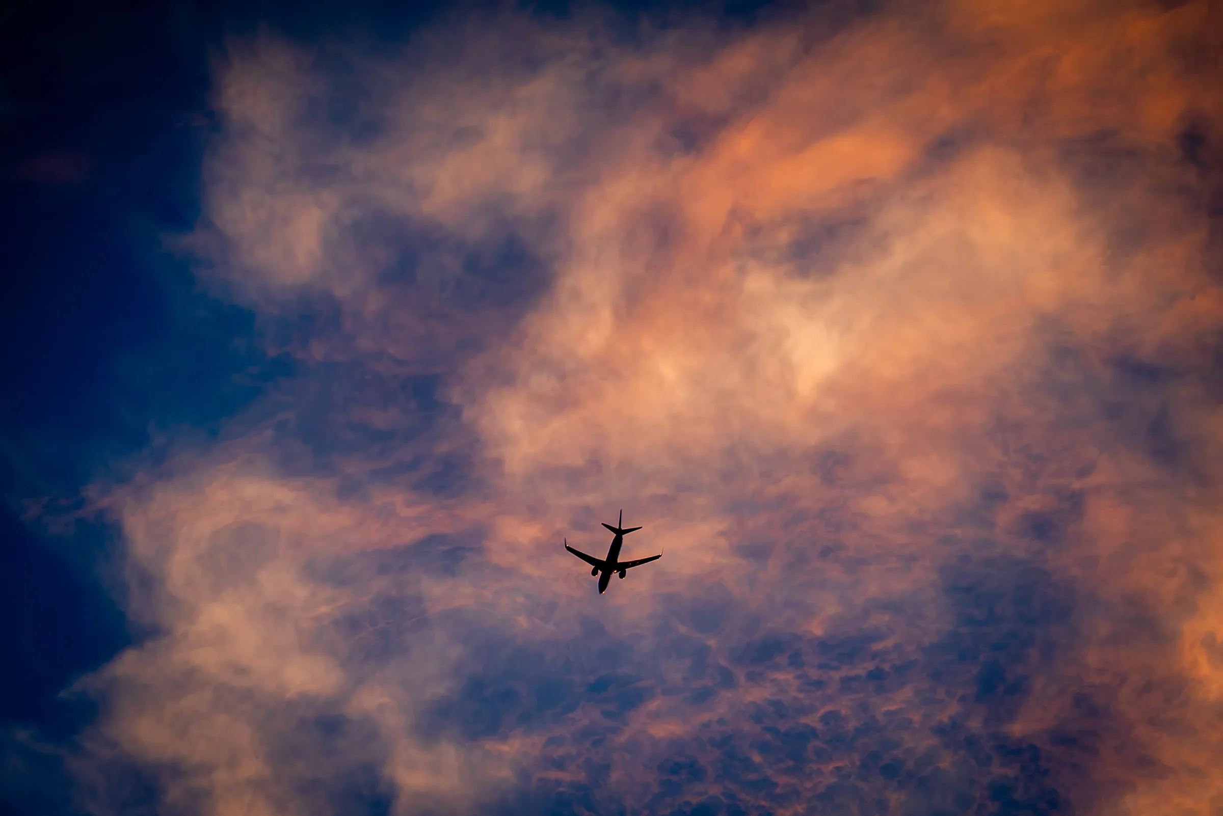 An airplane crossing burning sunset clouds