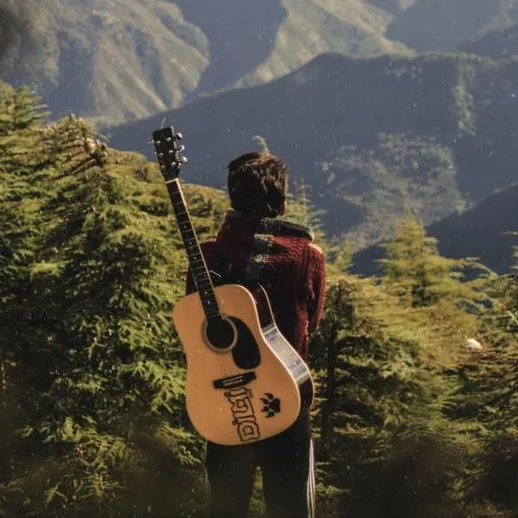Estel, seen from behind with a guitar, looking out over the mountains